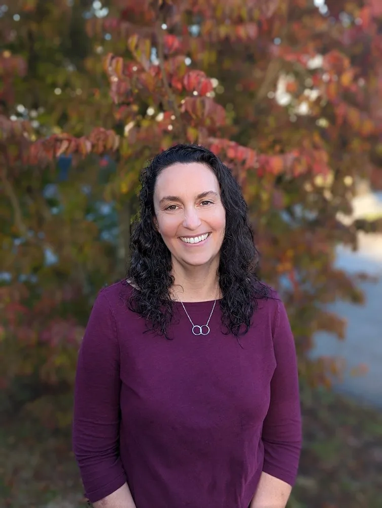 Julie Stein, Licensed Mental Health Counselor, smiling outdoors in front of autumn foliage